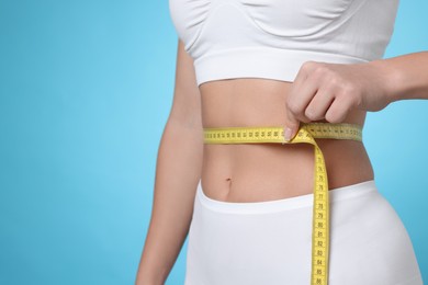 Photo of Weight loss. Woman measuring her slim waist with tape on light blue background, closeup. Space for text