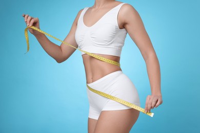 Photo of Weight loss. Woman measuring her slim waist with tape on light blue background, closeup