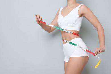 Photo of Weight loss. Woman measuring her slim waist with tape on light grey background, closeup. Space for text