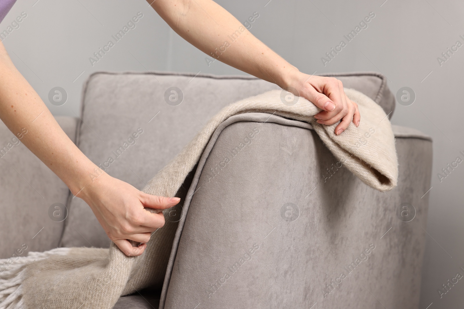 Photo of Female decorator arranging blanket onto armchair indoors, closeup