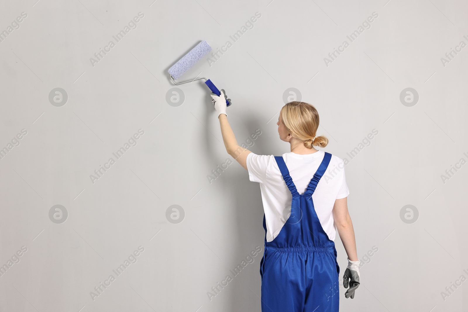 Photo of Female worker painting wall with roller indoors, back view. Space for text