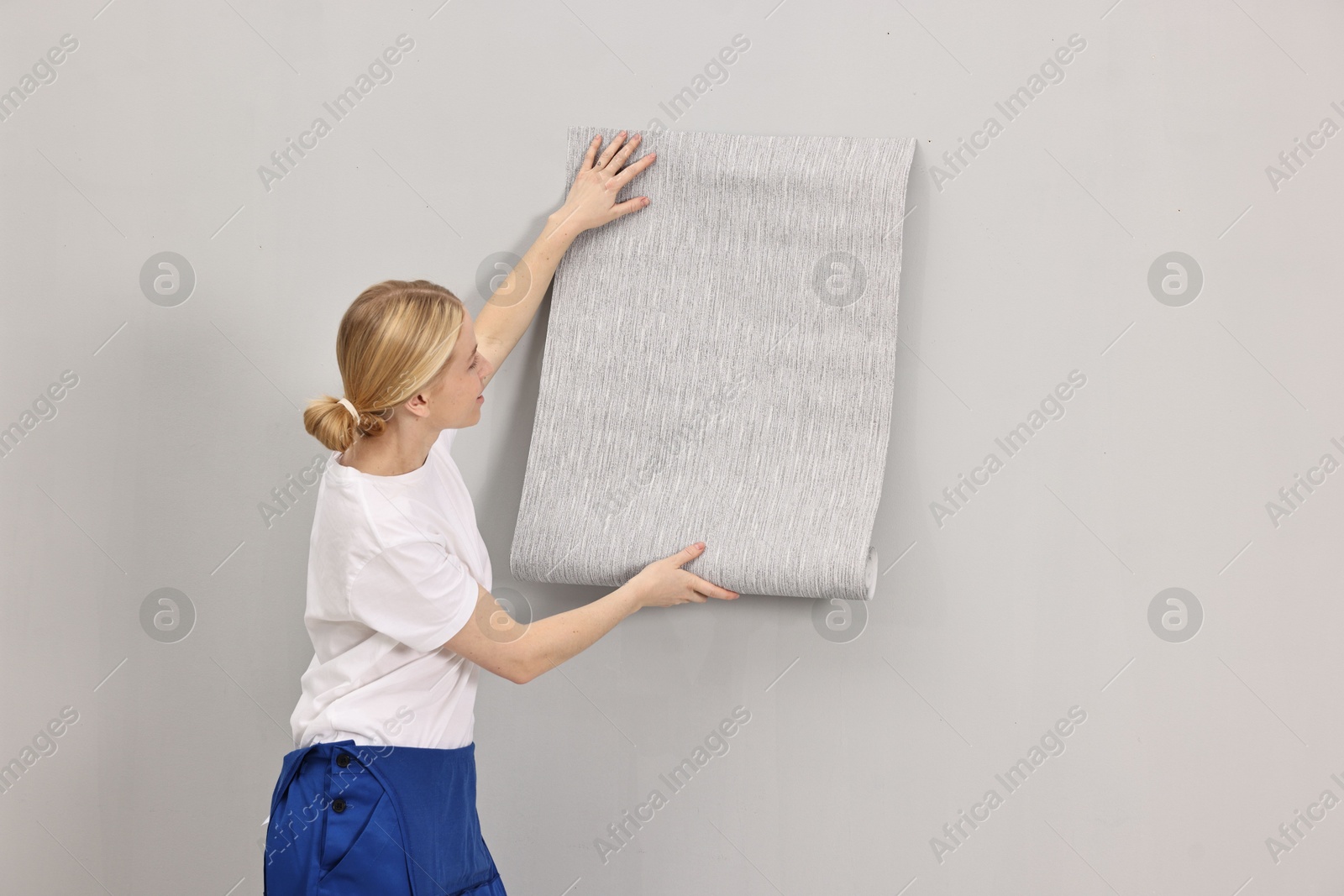 Photo of Female worker hanging grey wallpaper onto wall indoors. Space for text