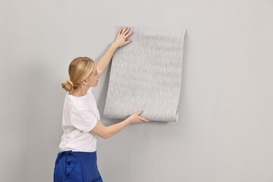 Photo of Female worker hanging grey wallpaper onto wall indoors. Space for text