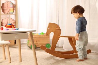 Photo of Cute little boy near wooden rocking horse at home