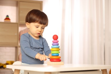 Photo of Cute little boy playing with toy pyramid at table indoors, space for text