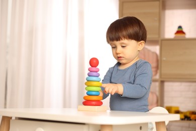 Photo of Cute little boy playing with toy pyramid at table indoors, space for text