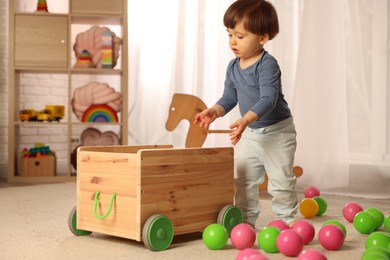 Photo of Cute little boy playing with wooden cart at home