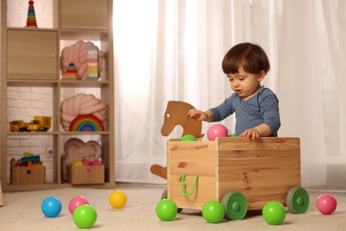 Photo of Cute little boy playing in wooden cart at home, space for text