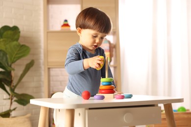 Photo of Cute little boy playing with toy pyramid at table indoors