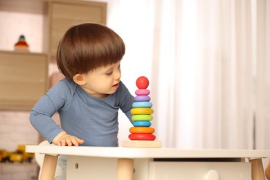 Photo of Cute little boy playing with toy pyramid at table indoors, space for text