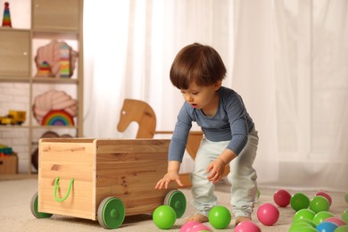 Photo of Cute little boy playing near wooden cart at home