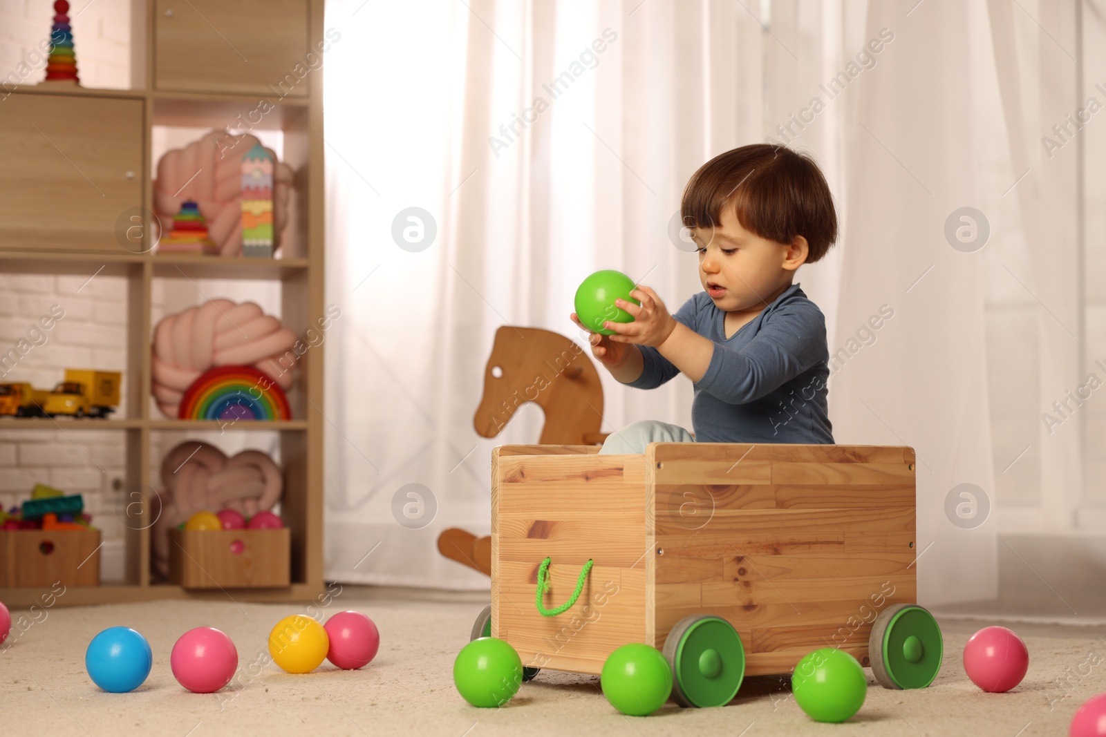 Photo of Cute little boy playing in wooden cart at home, space for text