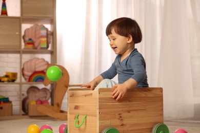 Photo of Cute little boy playing in wooden cart at home, space for text