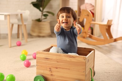 Photo of Cute little boy showing thumbs up in wooden cart at home