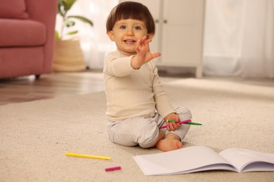 Photo of Cute little boy with felt pens and sketchbook on floor at home