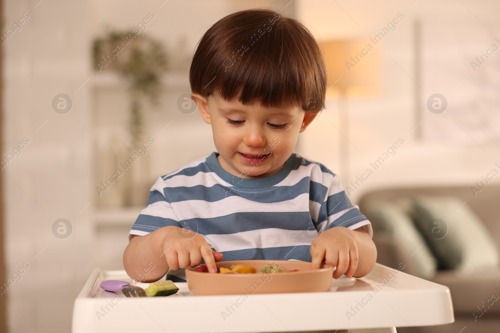 Photo of Cute little boy eating healthy food in high chair at home