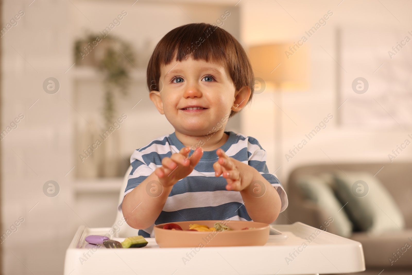 Photo of Cute little boy eating healthy food in high chair at home