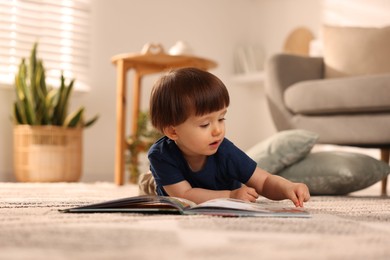 Photo of Cute little boy with book on floor at home