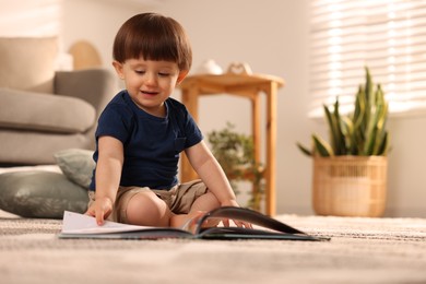 Photo of Cute little boy with book on floor at home, space for text