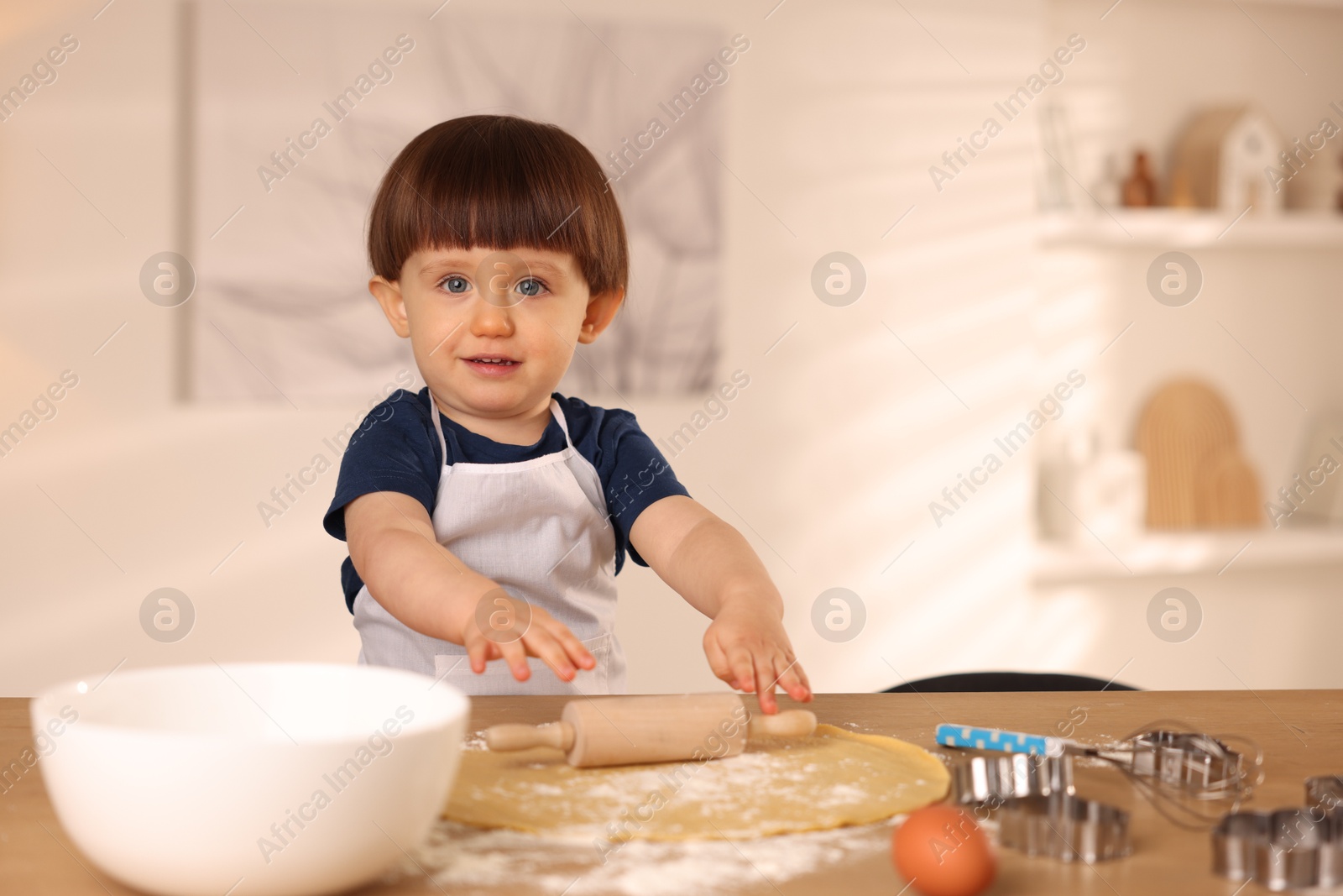 Photo of Cute little boy shaping dough with rolling pin at table indoors