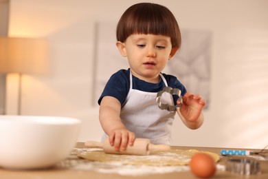 Photo of Cute little with rolling pin and cookie cutter at table indoors