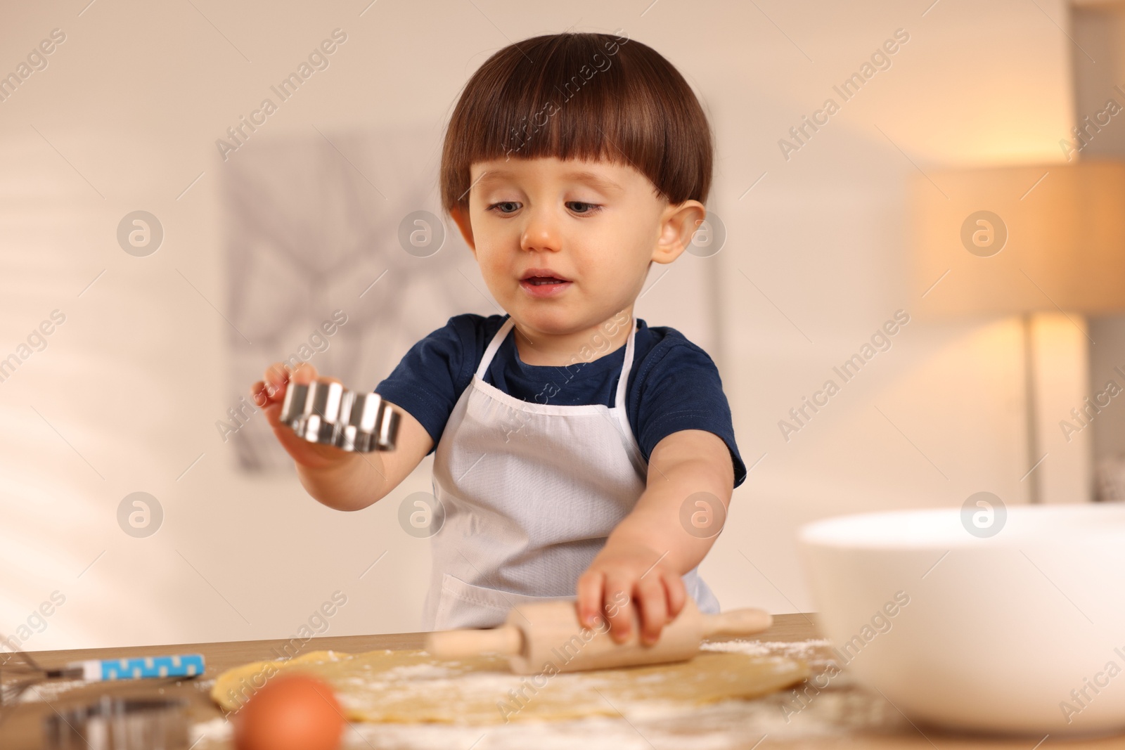 Photo of Cute little with rolling pin and cookie cutter at table indoors