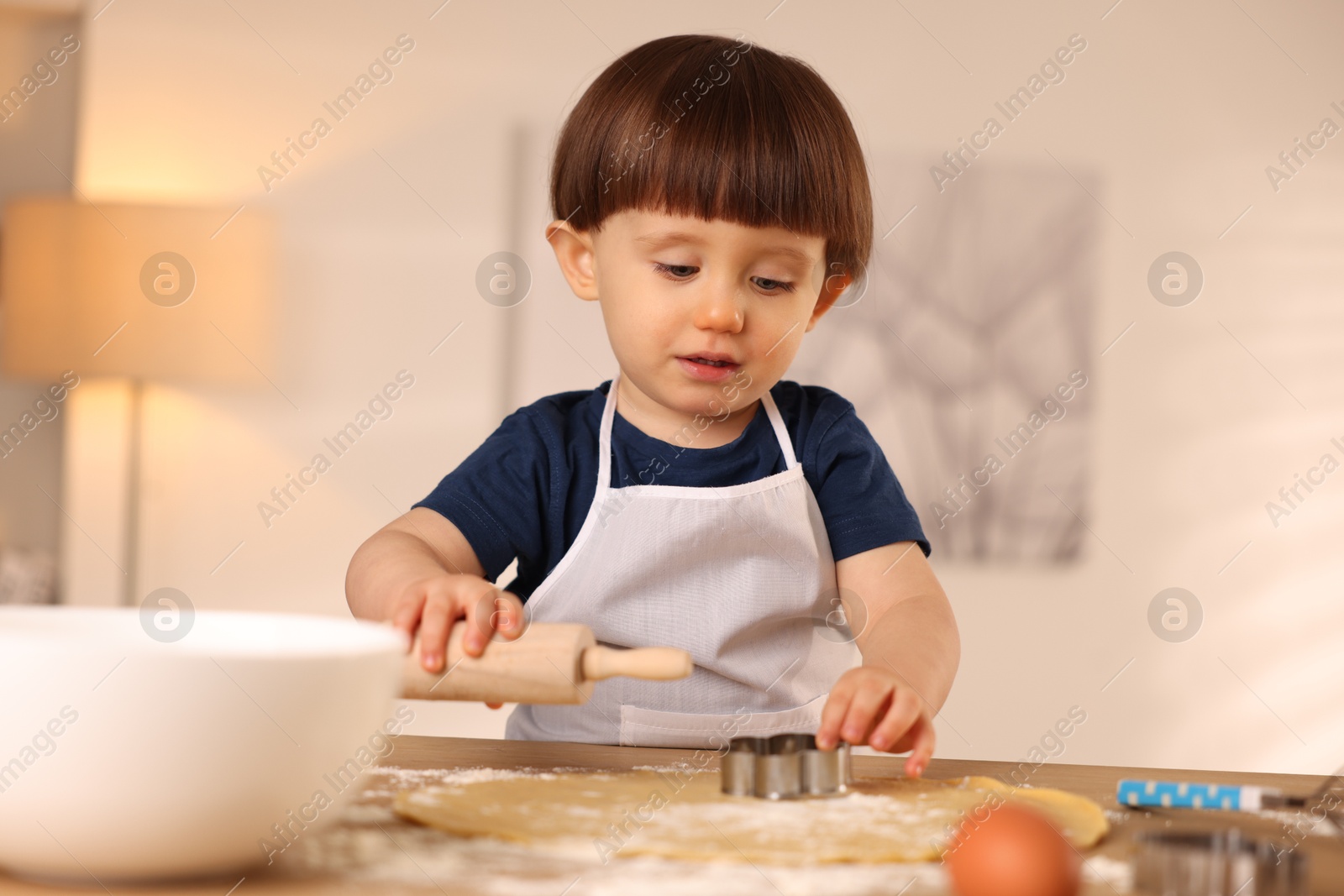 Photo of Cute little with rolling pin and cookie cutter at table indoors