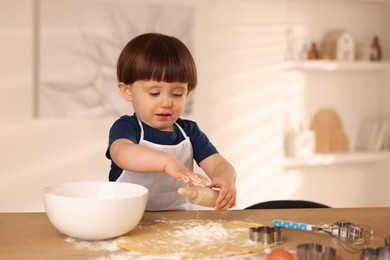 Photo of Cute little boy with rolling pin at table indoors, space for text