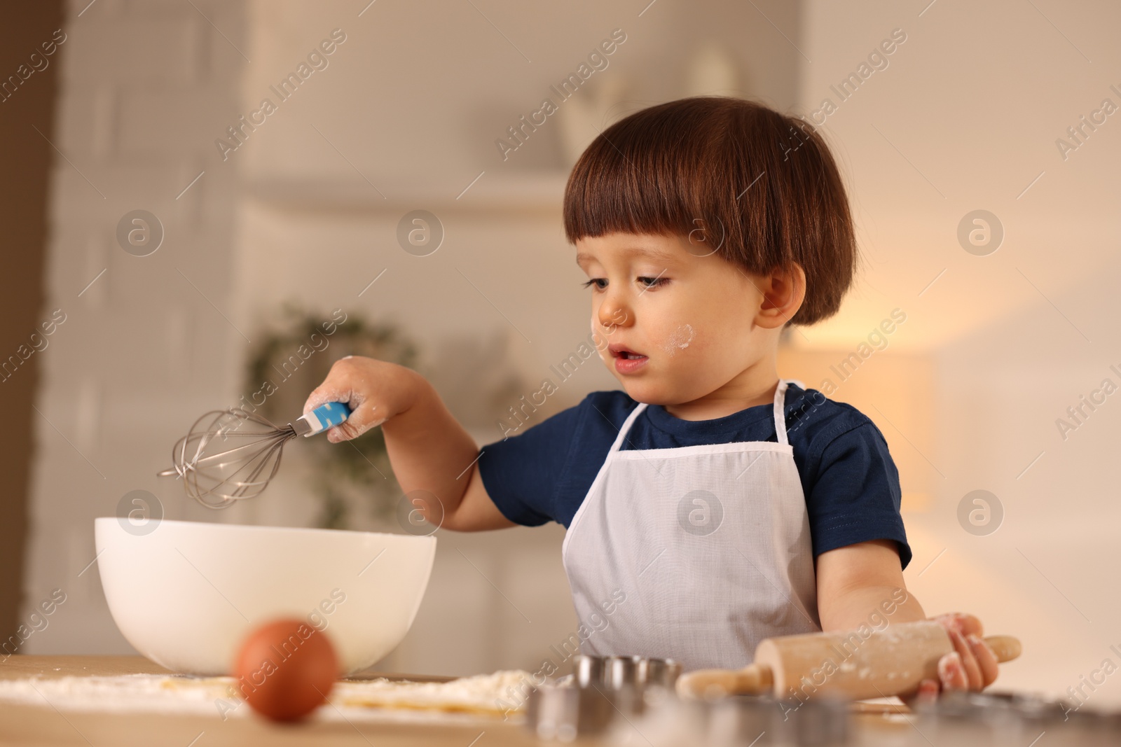 Photo of Cute little boy making dough at table indoors