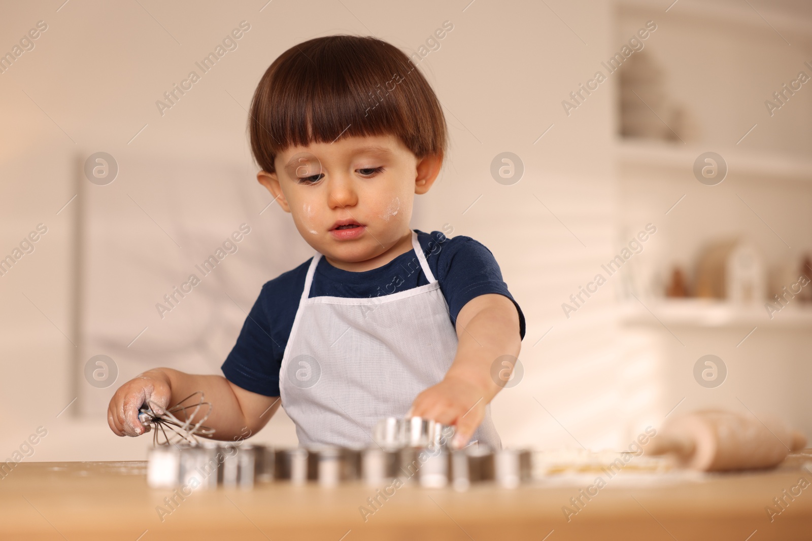 Photo of Cute little boy with cookie cutter and whisk at table indoors