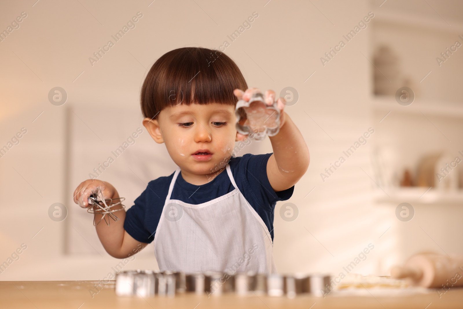 Photo of Cute little boy with cookie cutter and whisk at table indoors