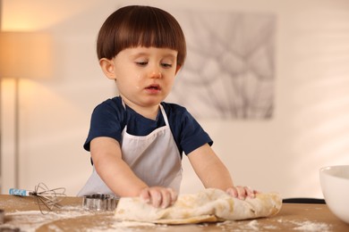 Photo of Cute little boy kneading dough at wooden table indoors