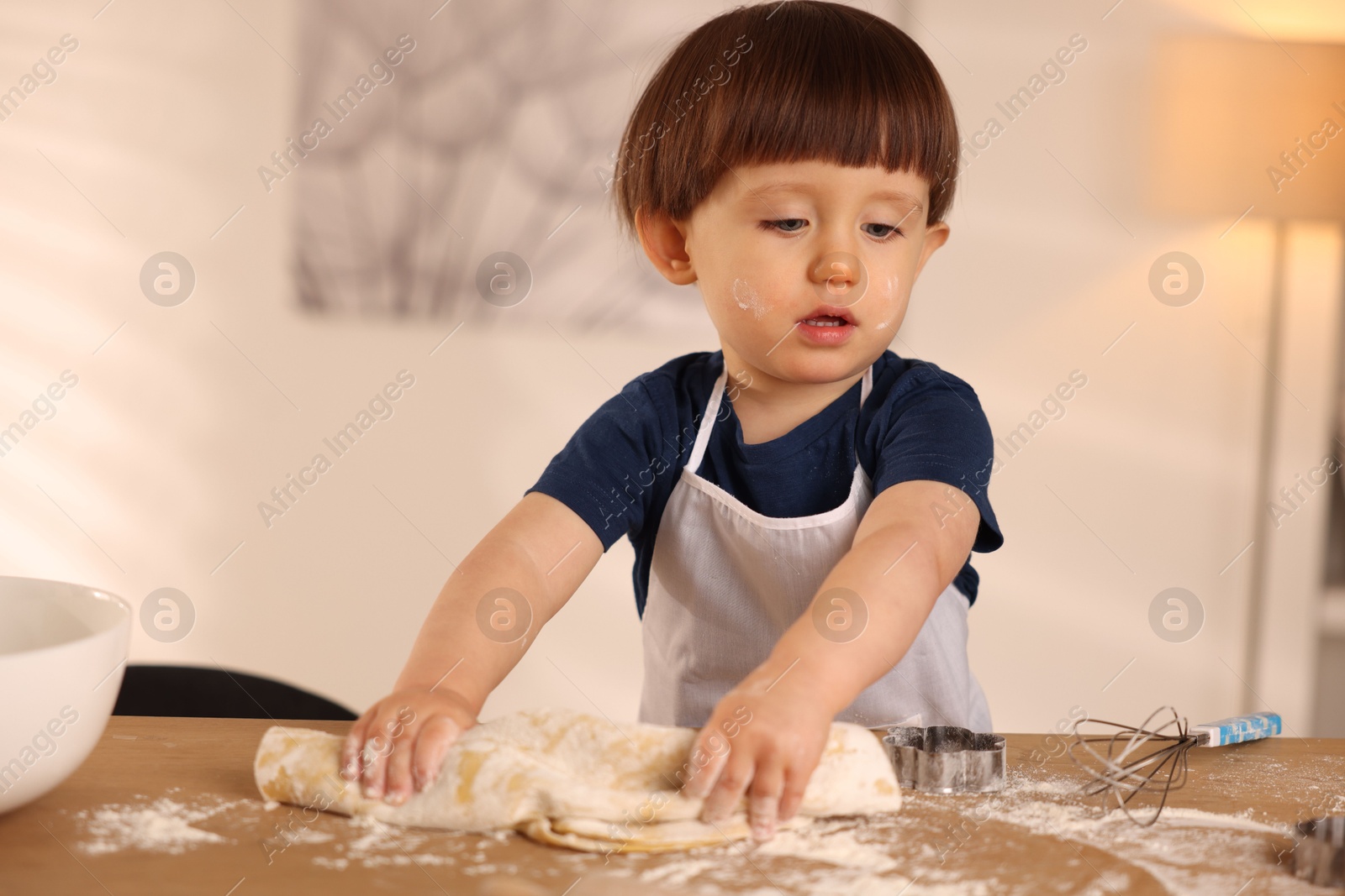 Photo of Cute little boy kneading dough at wooden table indoors