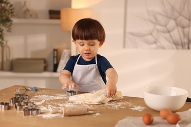 Photo of Cute little boy kneading dough at wooden table indoors