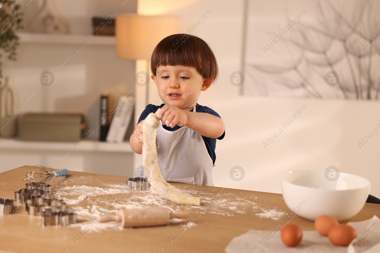 Photo of Cute little boy kneading dough at wooden table indoors