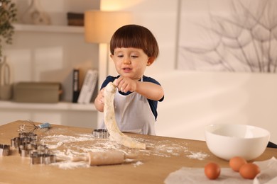 Photo of Cute little boy kneading dough at wooden table indoors