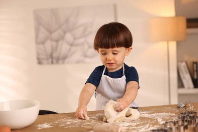 Photo of Cute little boy kneading dough at wooden table indoors