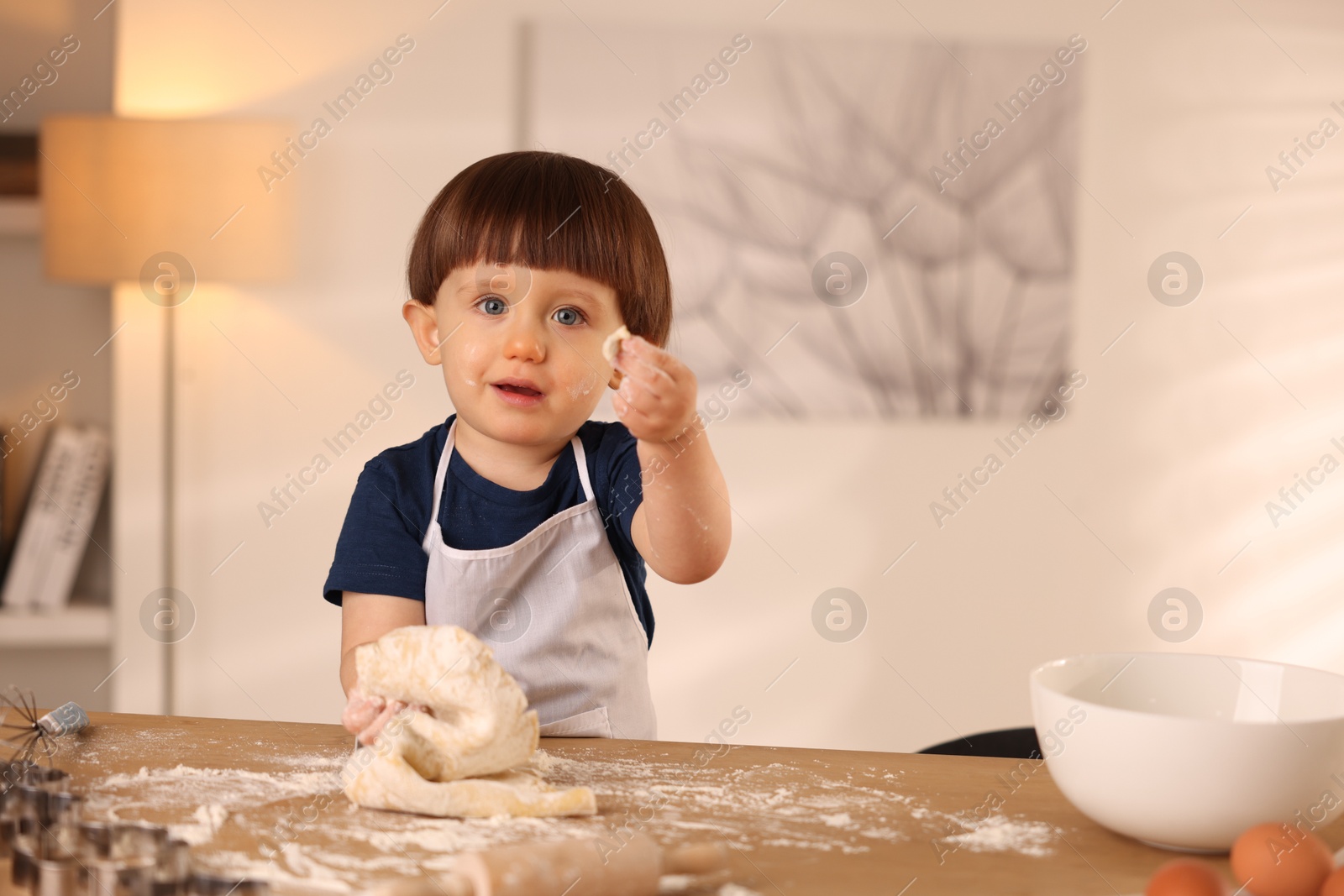 Photo of Cute little boy kneading dough at wooden table indoors, space for text