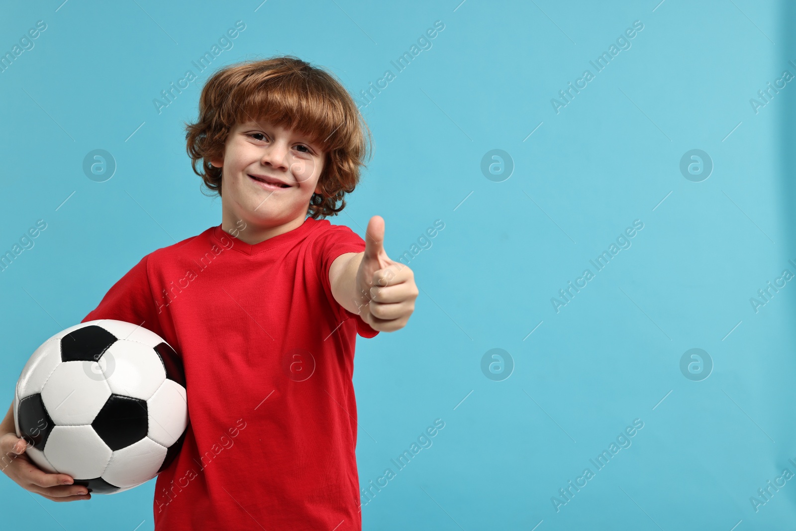 Photo of Little boy with soccer ball showing thumbs up on light blue background, space for text