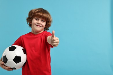 Photo of Little boy with soccer ball showing thumbs up on light blue background, space for text