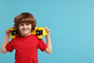 Little boy with penny board on light blue background, space for text