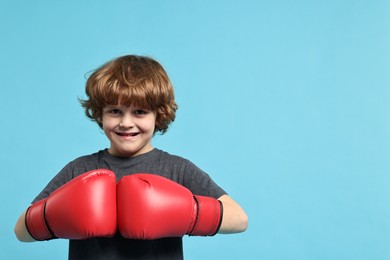 Photo of Little boy with boxing gloves on light blue background, space for text