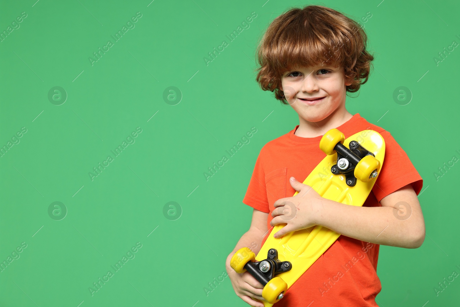 Photo of Little boy with penny board on light green background, space for text