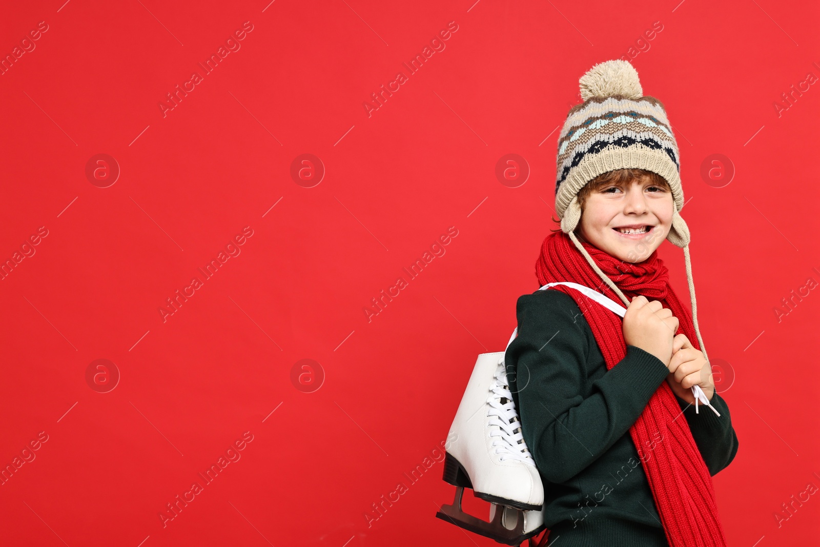 Photo of Little boy in hat with ice skates on red background, space for text