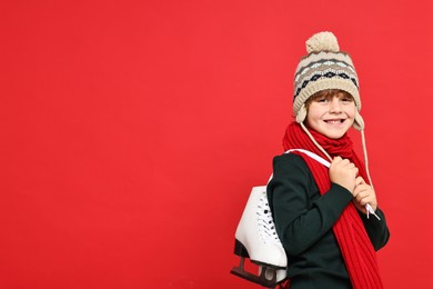 Little boy in hat with ice skates on red background, space for text