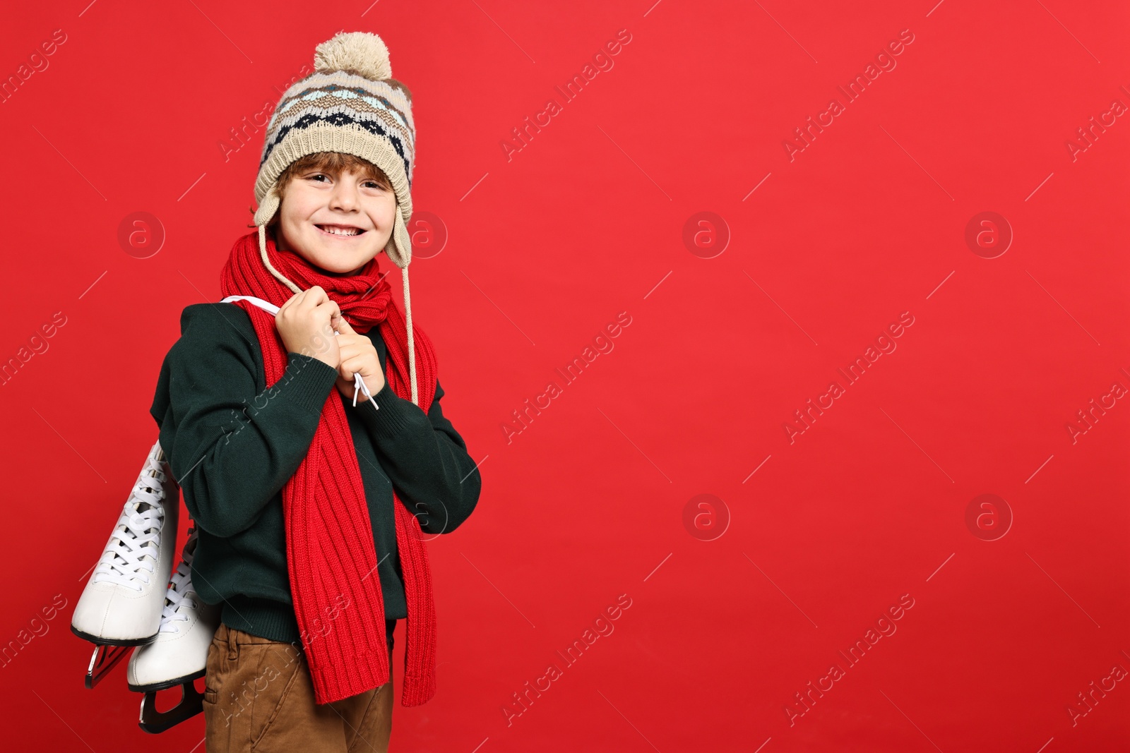 Photo of Little boy in hat with ice skates on red background, space for text