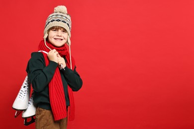 Little boy in hat with ice skates on red background, space for text