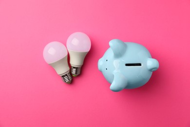 Photo of Piggy bank and light bulbs on pink background, flat lay. Energy saving concept