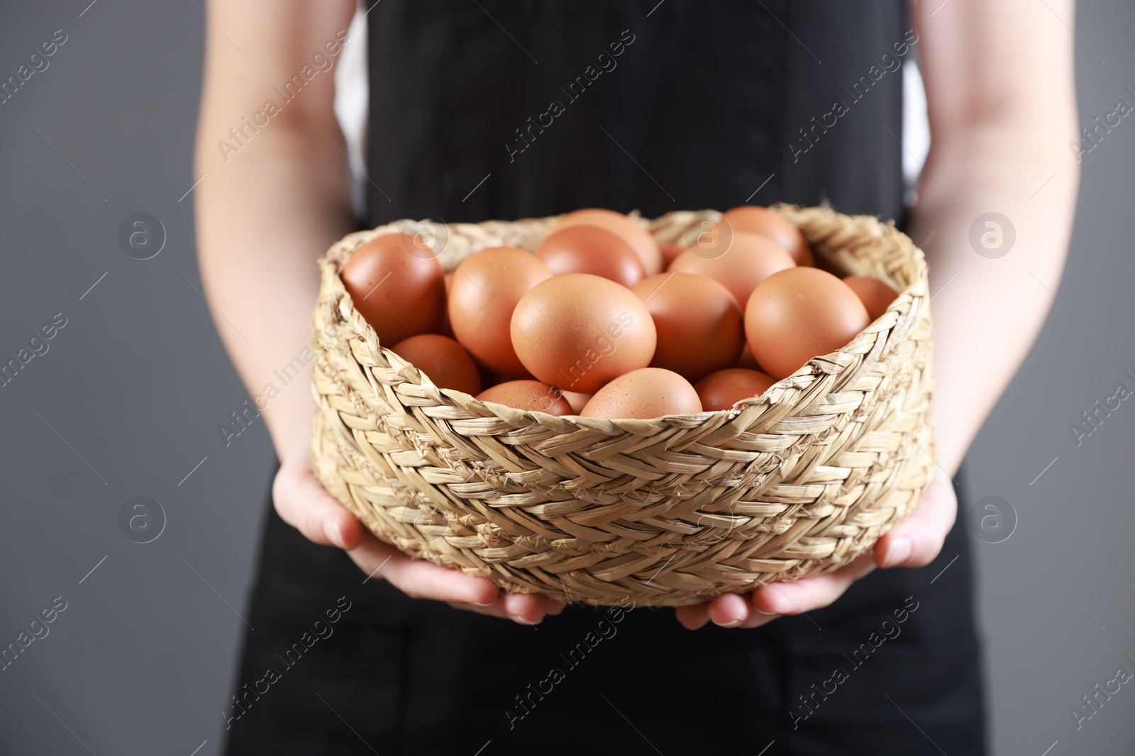 Photo of Woman with basket of eggs on grey background, closeup