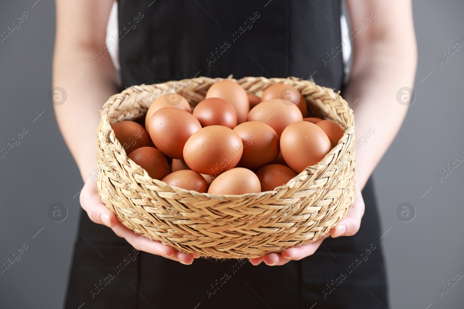 Photo of Woman with basket of eggs on grey background, closeup